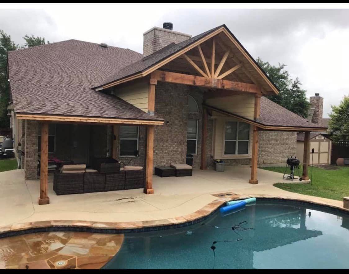 Backyard patio with pool, covered seating area, and brick exterior on a cloudy day.