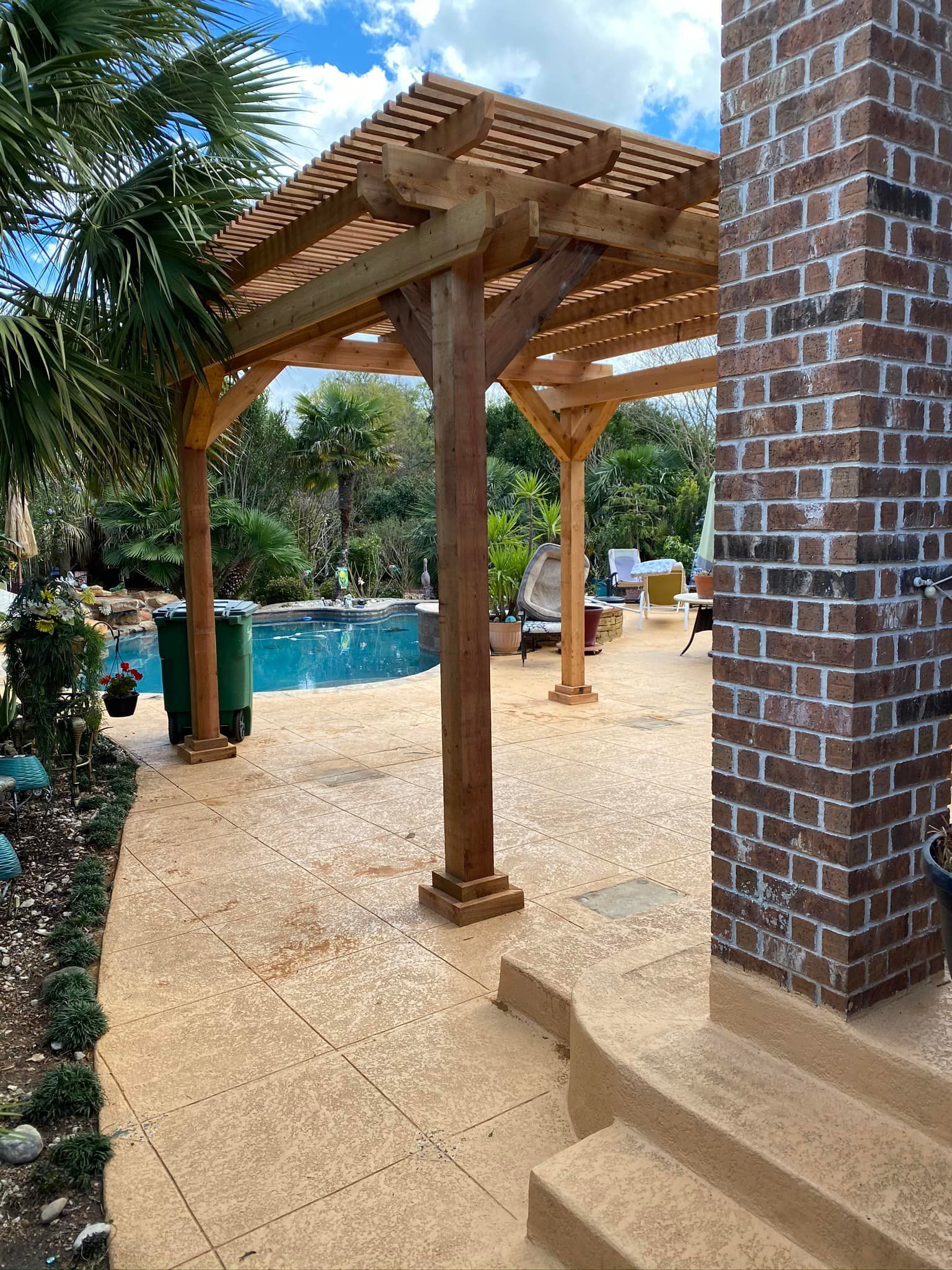 Wooden pergola near a pool and brick structure. The sky is blue.