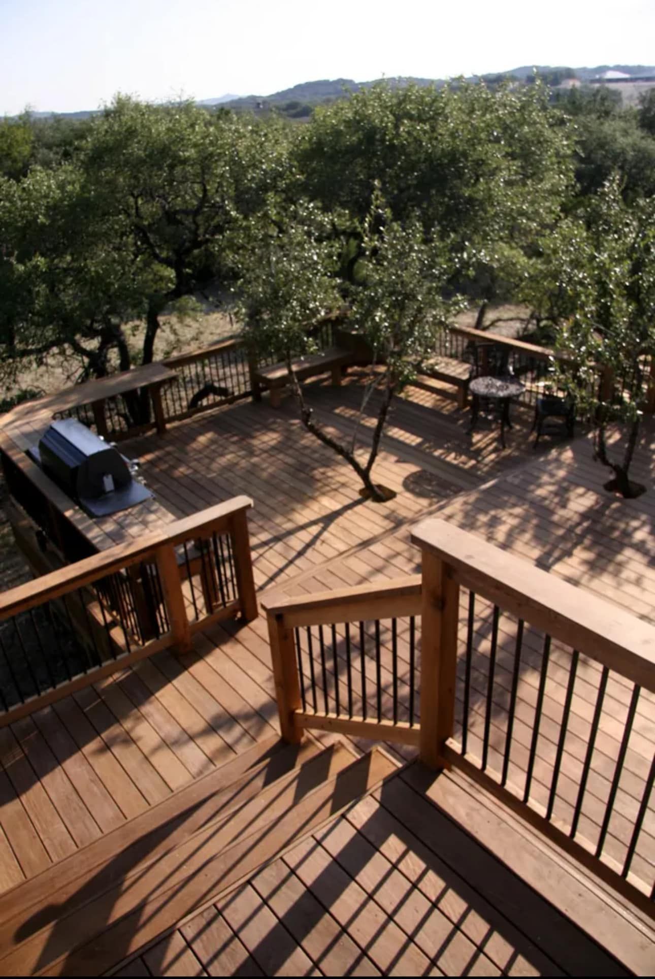 Wooden deck with grilling area, tables, and trees in a natural setting.