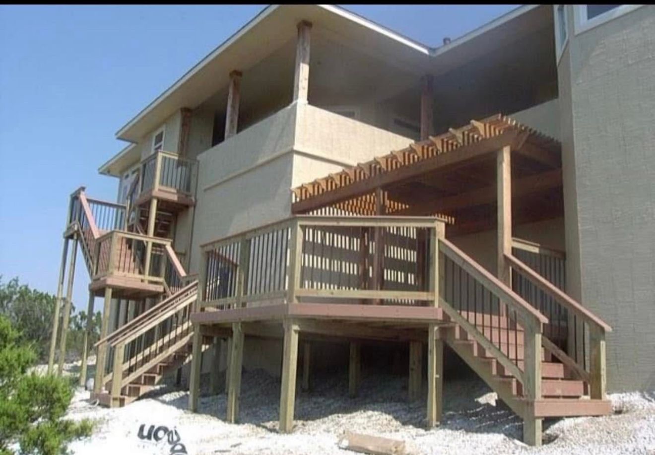 Exterior view of a multi-level deck attached to a light-colored building. Wooden stairs and railings are visible.