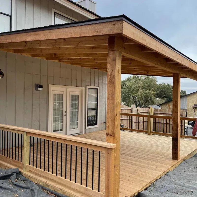 Wooden deck with attached pergola, French doors, black railing.
