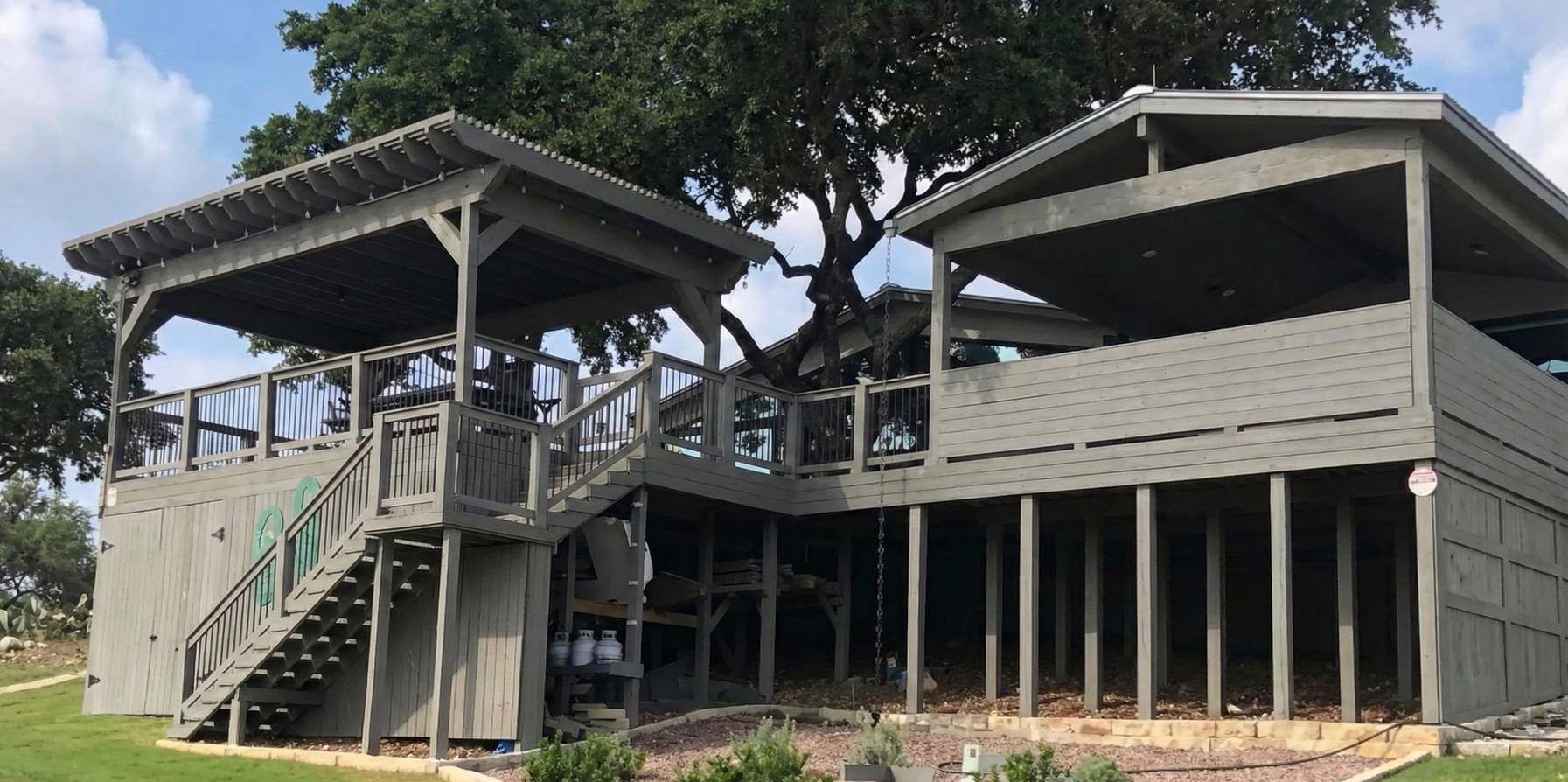 Wooden deck extension with gabled roof, attached to a brick house, under a partly cloudy sky.
