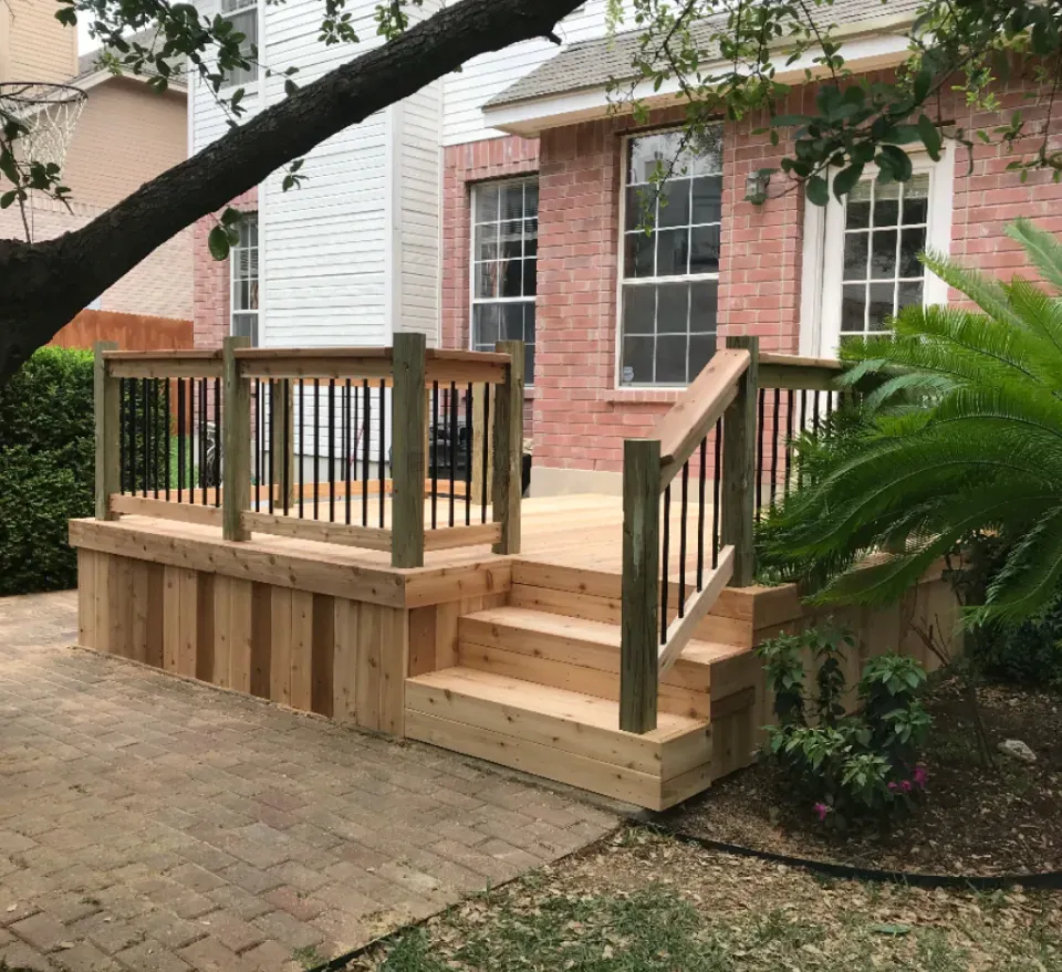 Wooden deck with steps, black railing, and a brick house in the background.