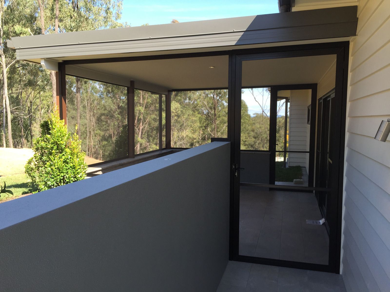 Screened porch with dark framing, gray roof, and low concrete wall, with trees in the background.