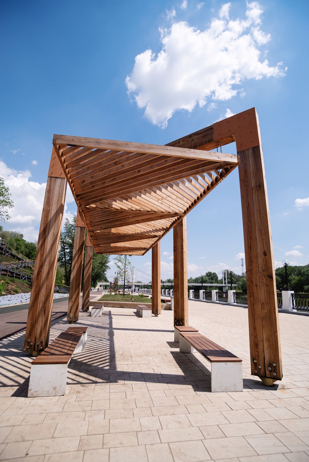 Wooden pergola with benches beneath, blue sky and clouds in the background.