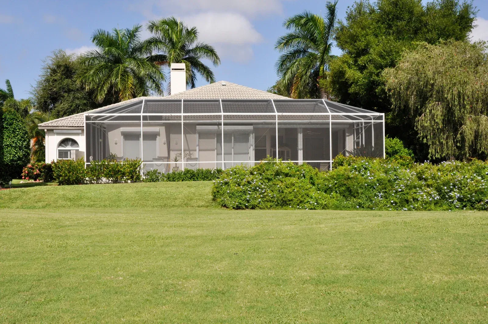 House with screened porch, surrounded by green grass and landscaping, under a blue sky.