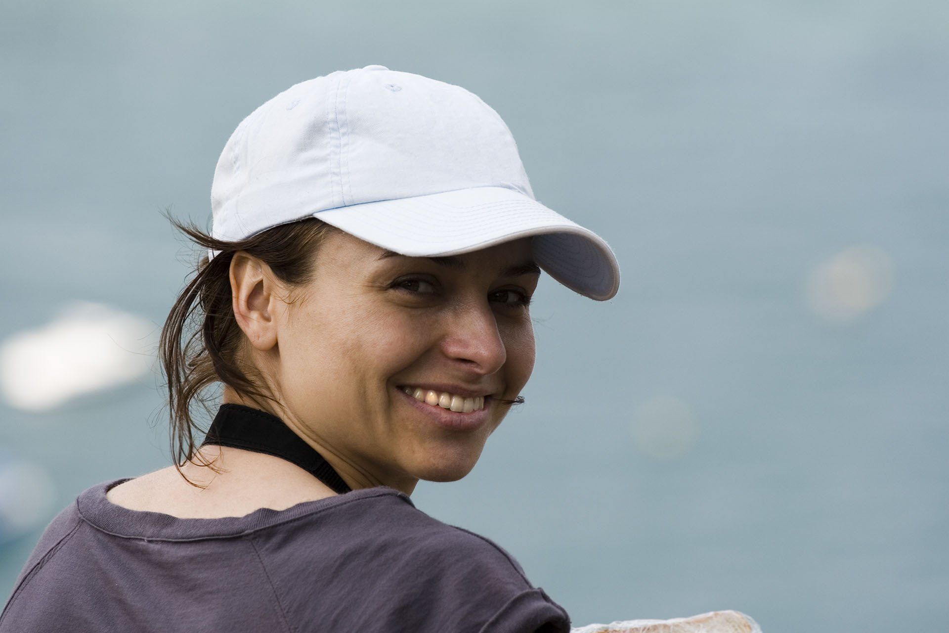 A woman wearing a white baseball cap is smiling