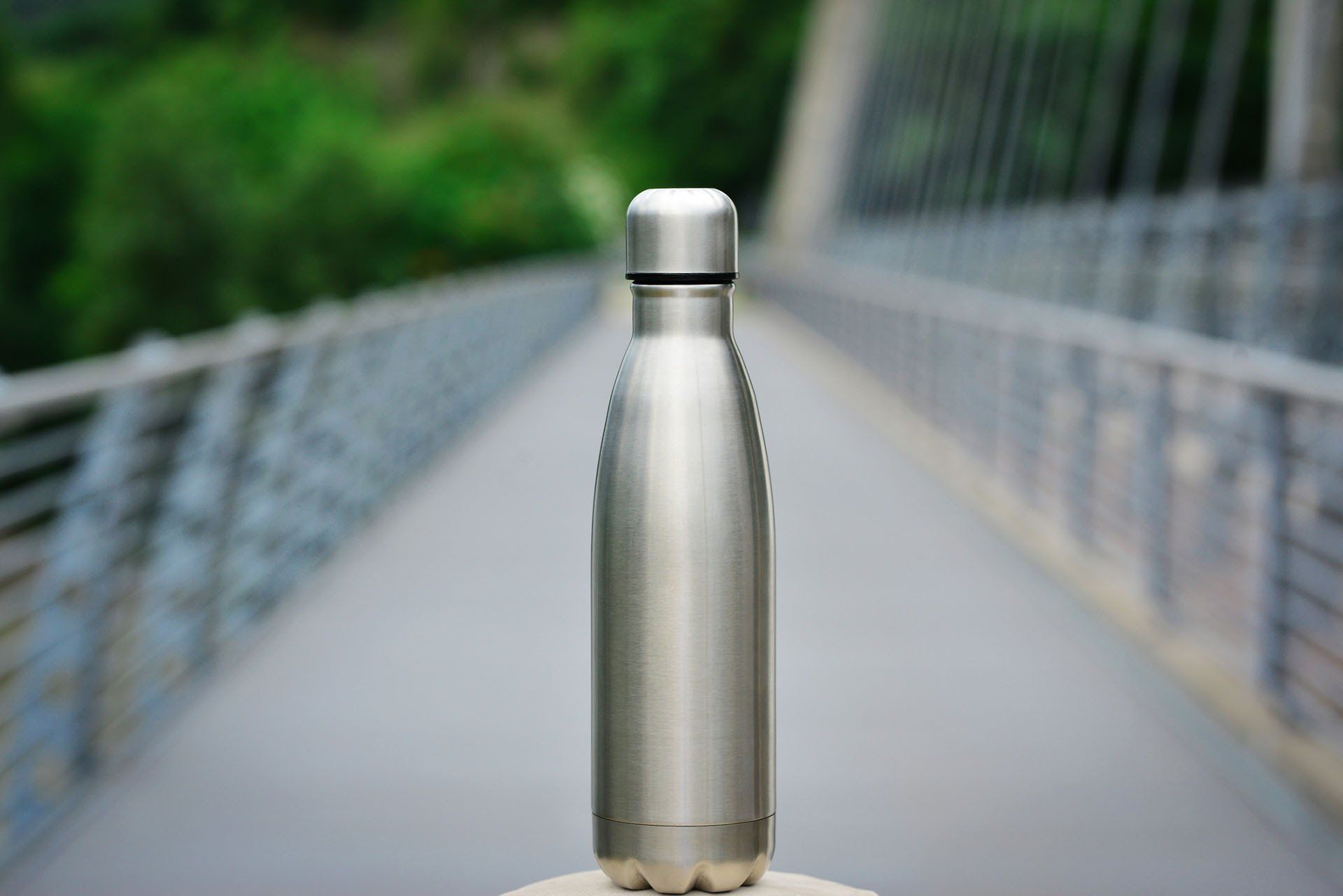 A stainless steel water bottle is sitting on a bridge.