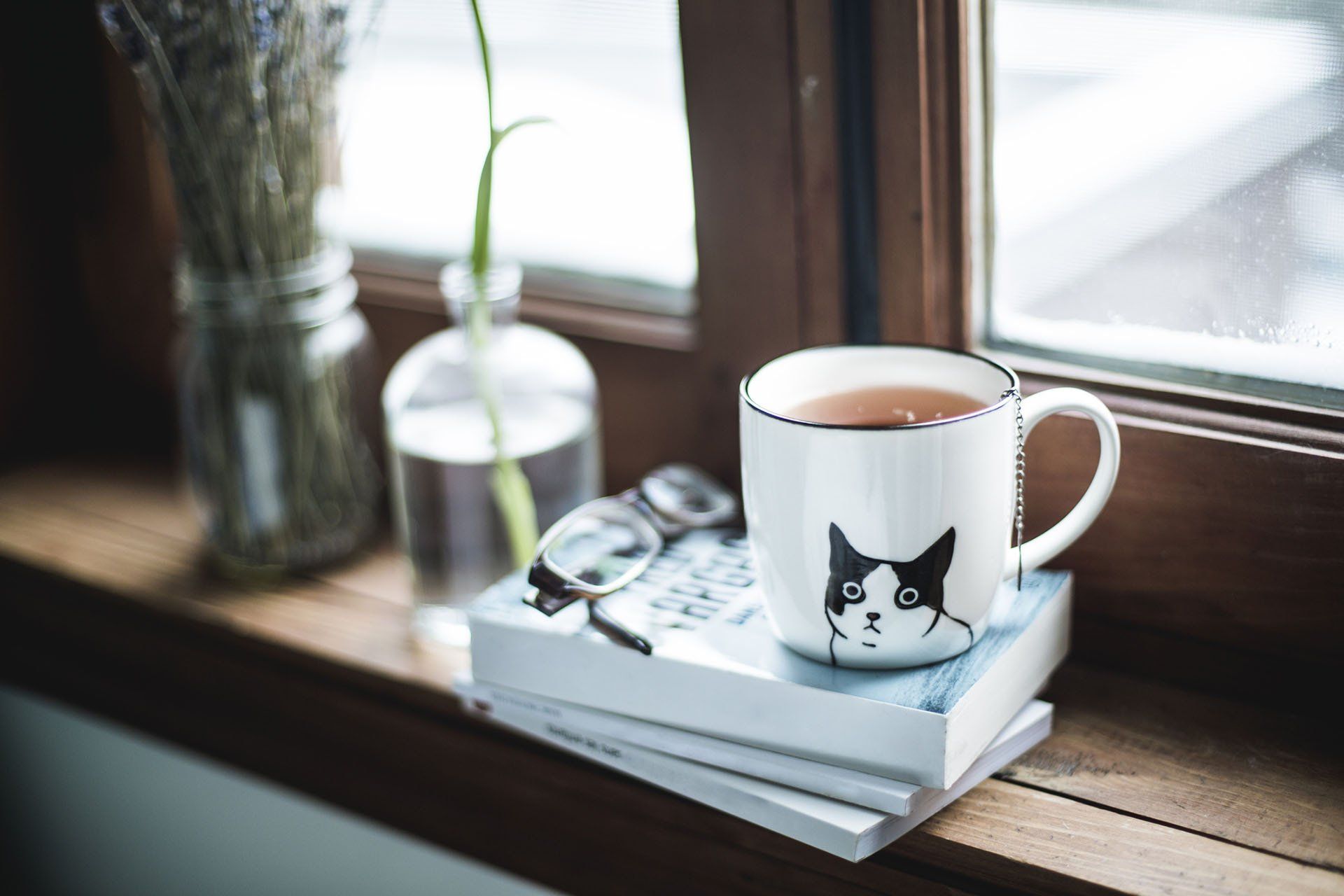 A cup of tea is sitting on top of a stack of books on a window sill.