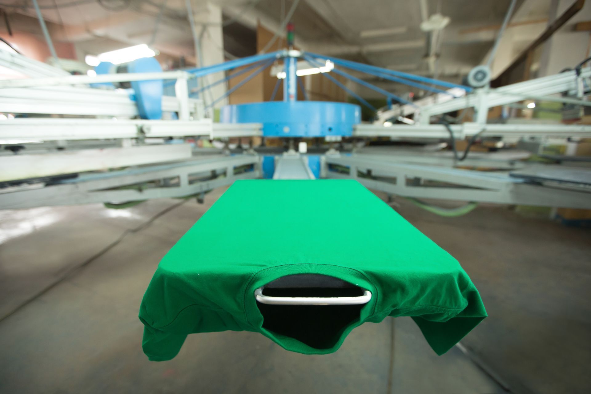 A green t-shirt is being printed on a machine in a factory.