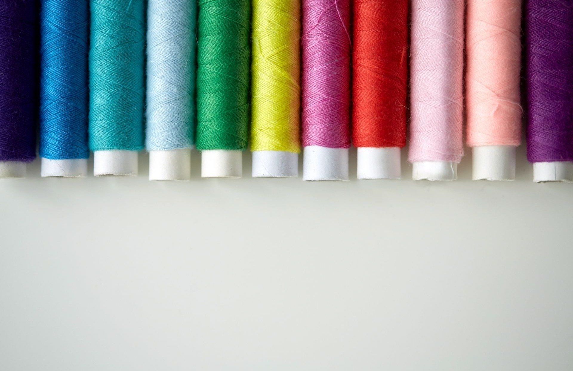 A row of colorful spools of thread on a white surface.