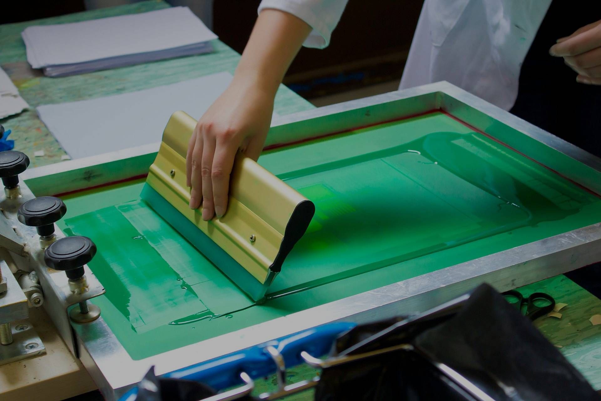 A person is using a squeegee on a screen printing machine.