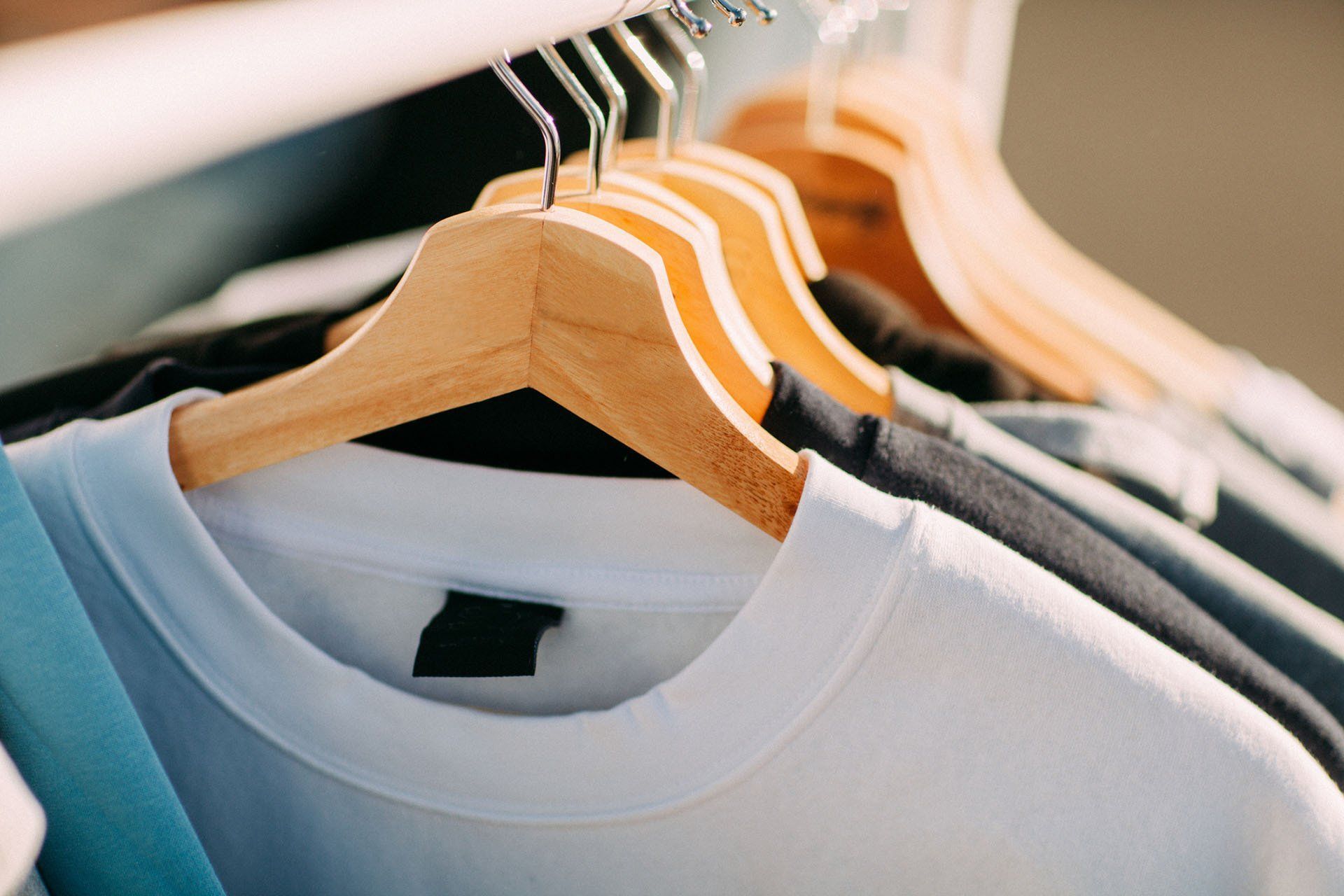 A row of t-shirts hanging on wooden hangers in a closet.