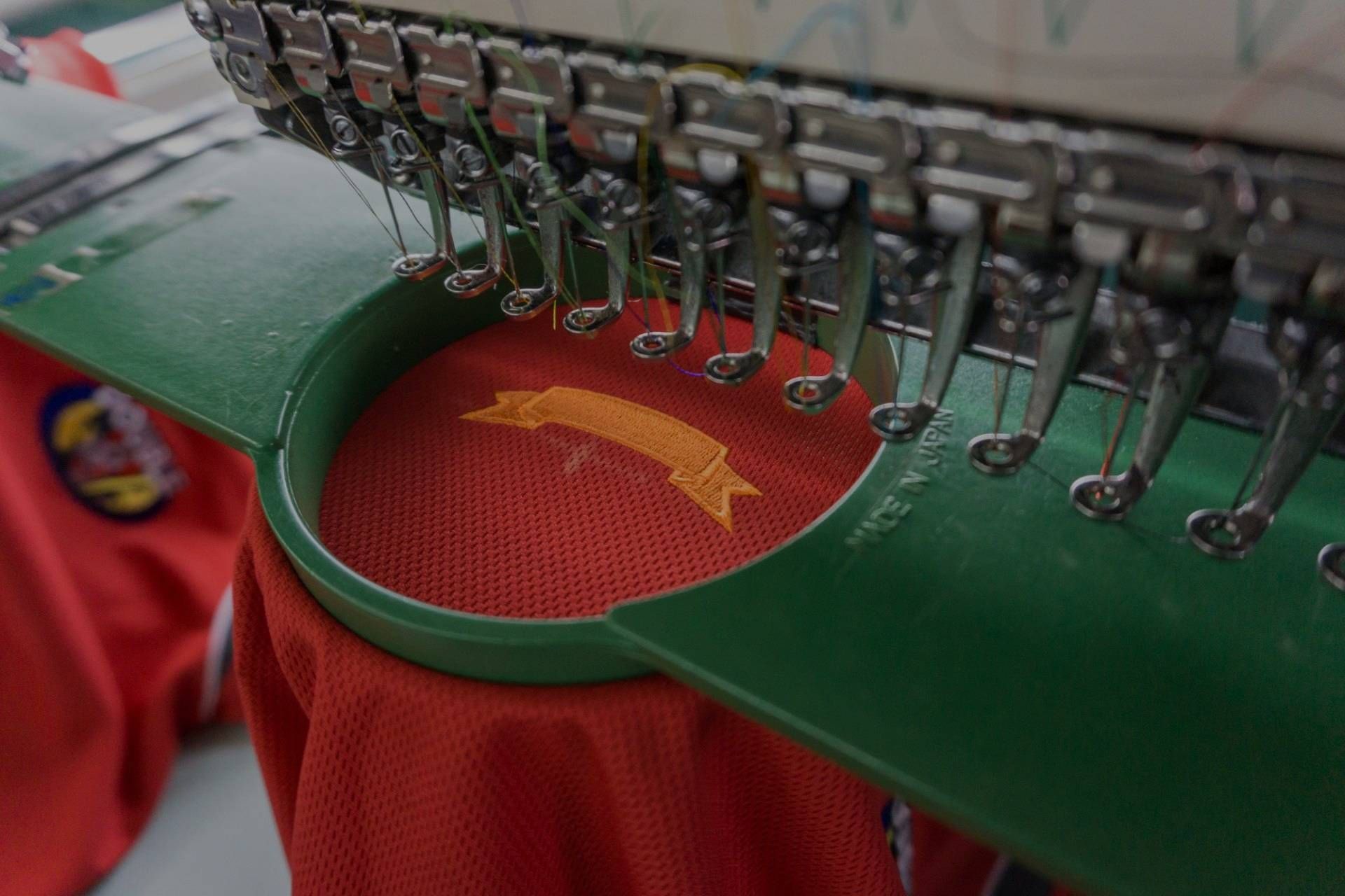 A close up of a machine that is embroidery on a red shirt.