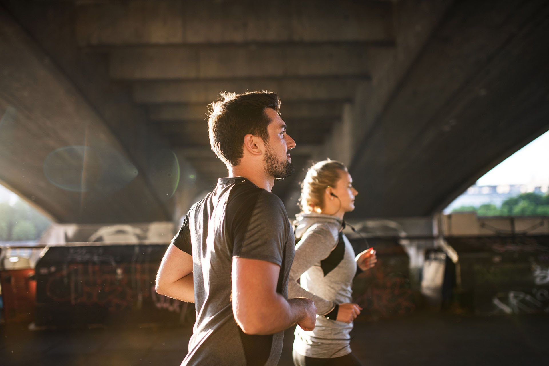 A man and a woman are running under a bridge.