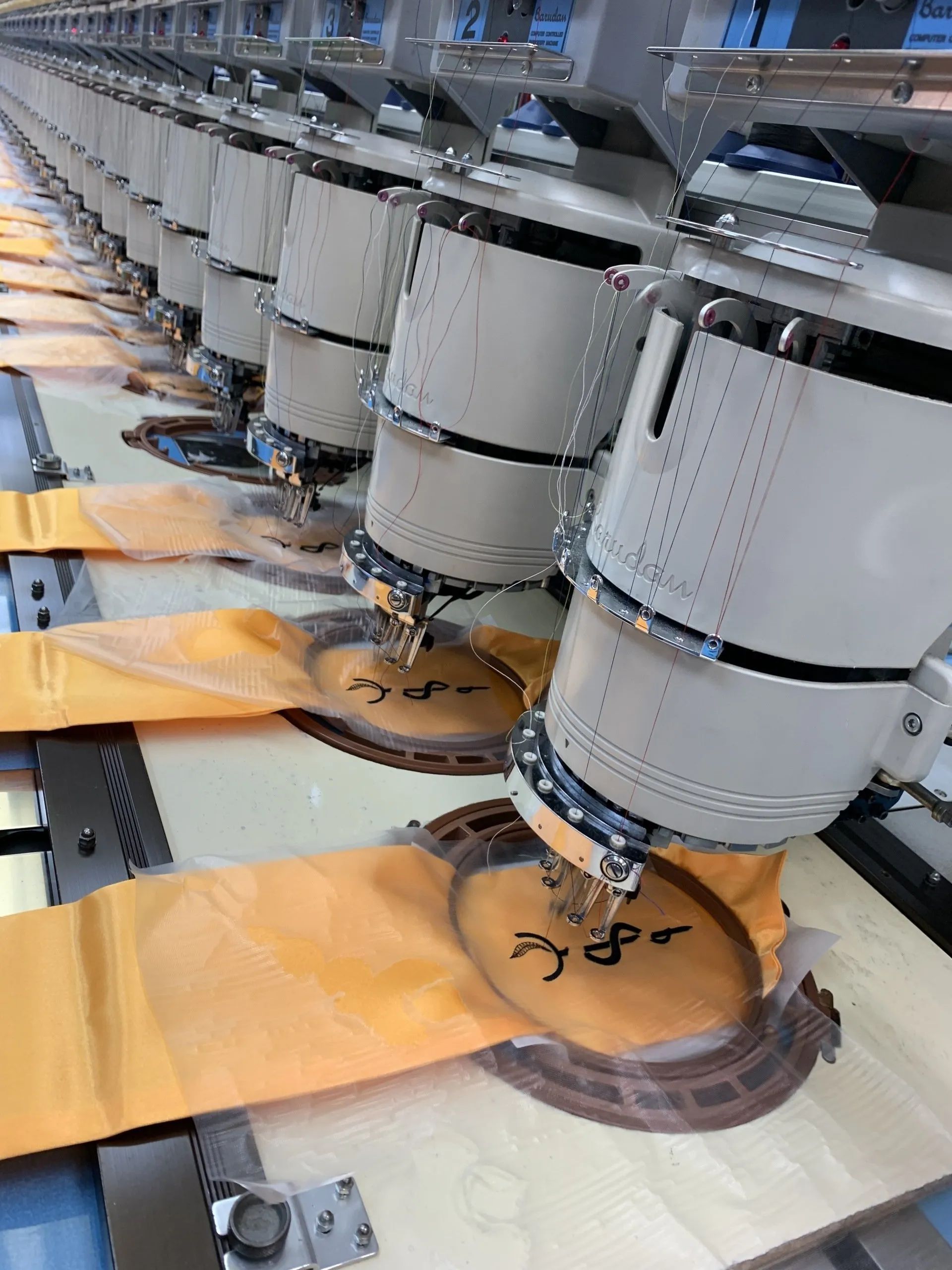 A row of embroidery machines are working on a piece of fabric.