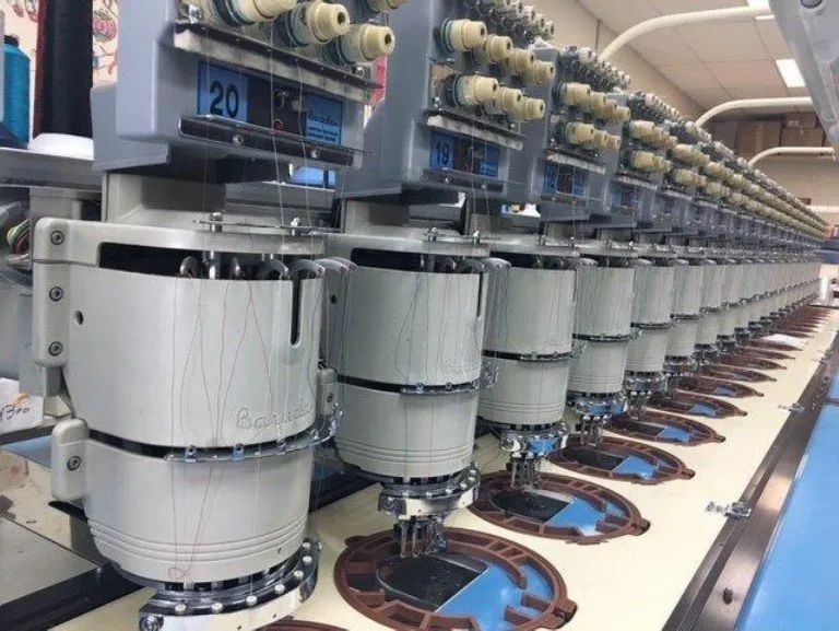 A row of embroidery machines are lined up in a factory.