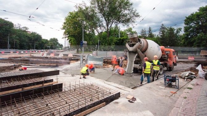 Construction workers around a large bulldozer on a roadwork site with rebar and concrete forms