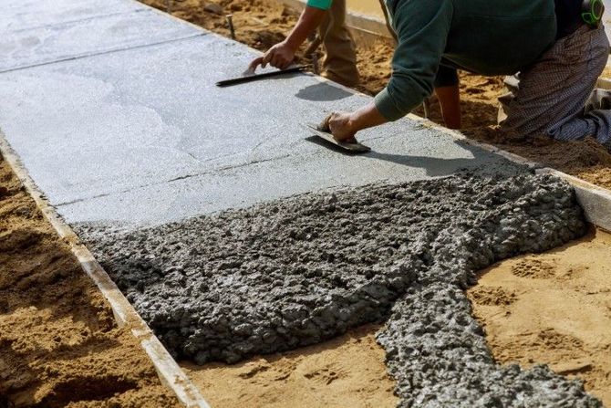 Workers pouring and smoothing wet concrete on a sidewalk construction site