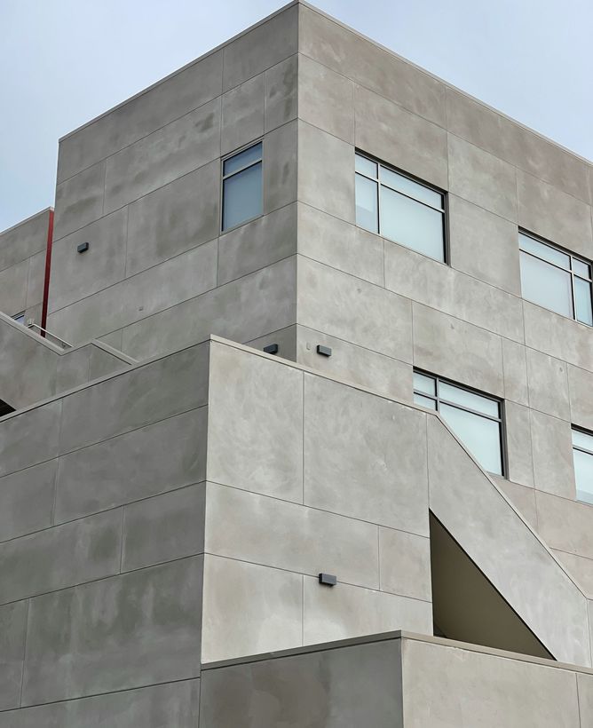 Concrete modern building facade with small windows and an angular exterior stairwell under a cloudy sky
