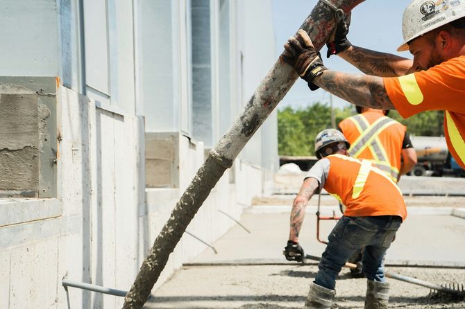 Construction workers in orange vests pouring concrete at a building site