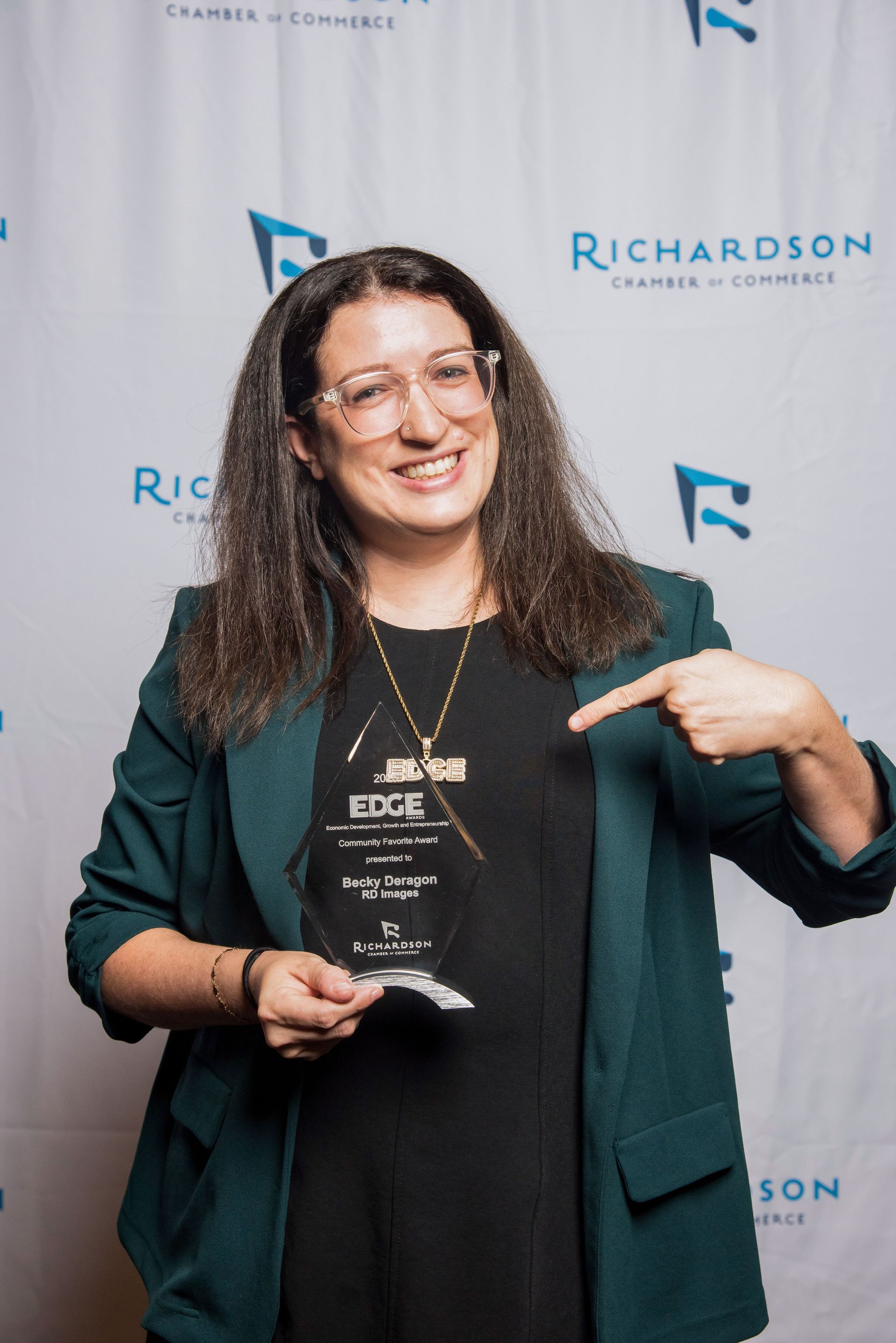 A graduate in a cap and gown with a red and gold stole and medals, standing outdoors and smiling at the camera.