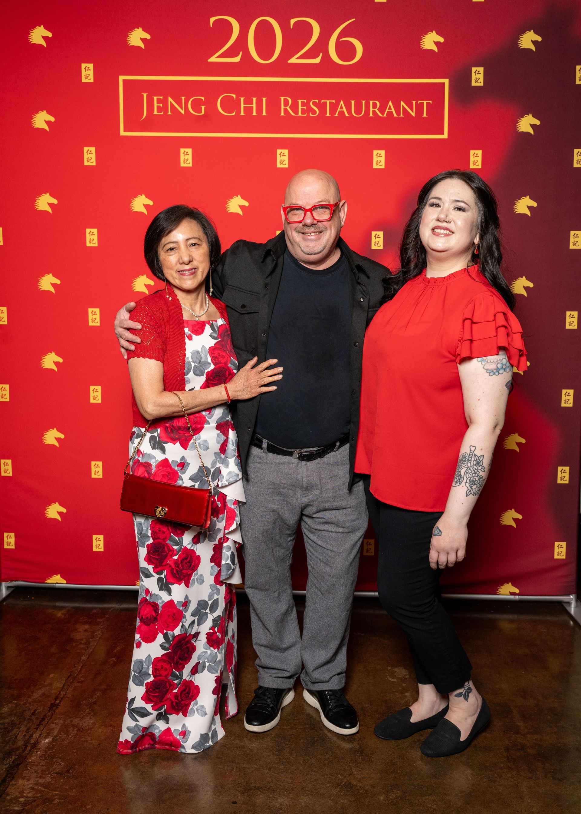 Three people pose for a photo in front of a red 