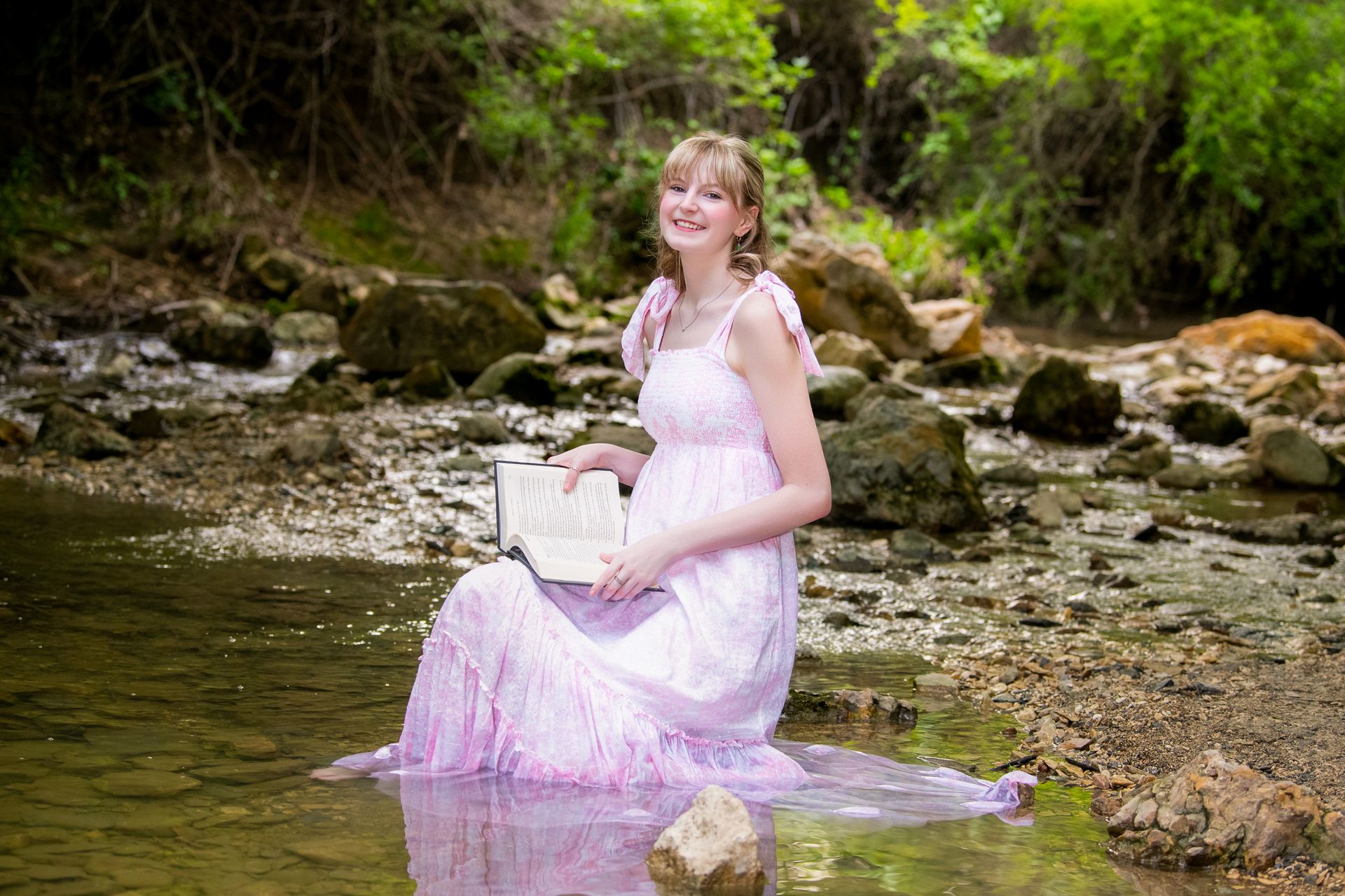 A person in a black suit and white shirt standing on a paved plaza in front of a modern, tall gray building and trees.