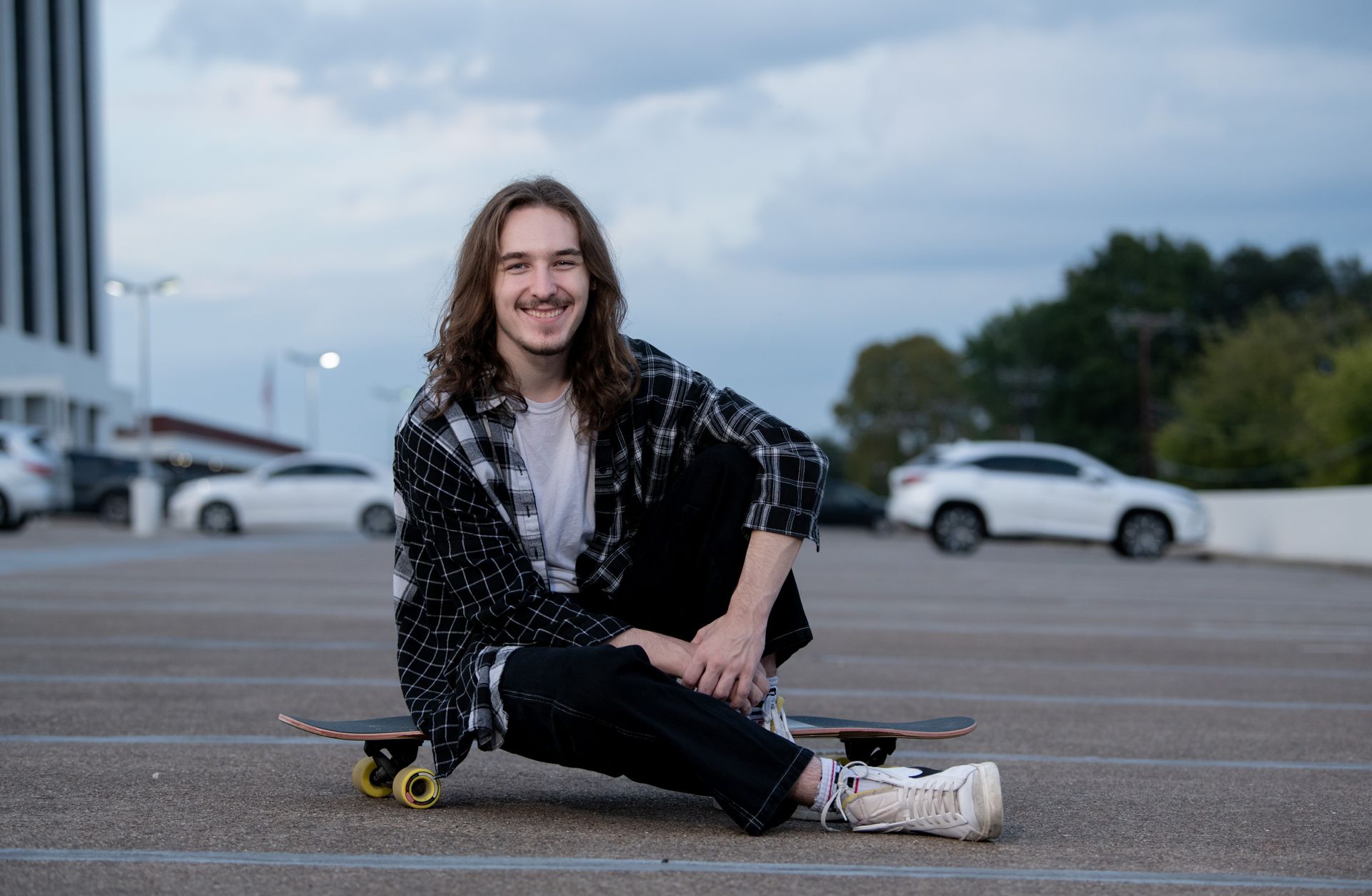 A student in a graduation cap and gown with a red stole stands centered in front of a colorful, graffiti-covered wall.