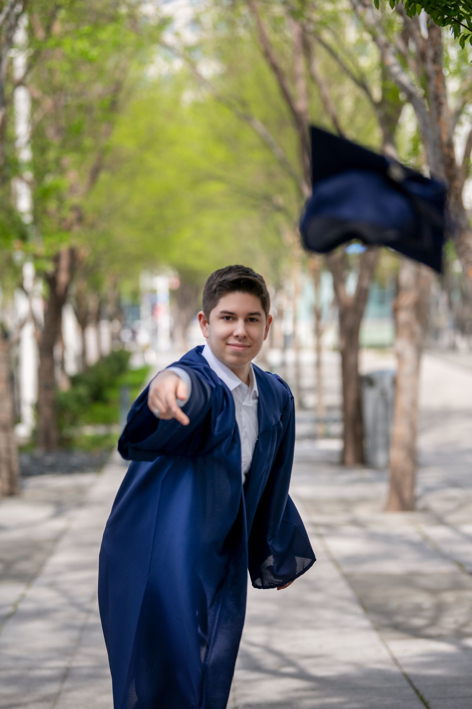A person smiling while sitting on a stone block in front of a cascading water fountain, wearing a green cardigan and jeans.