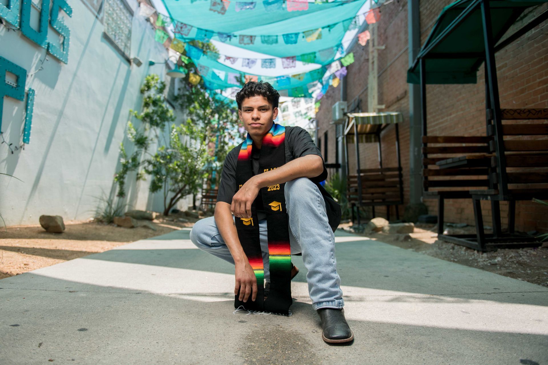 A person in a denim dress stands on a lawn with arms outstretched, posing in front of a domed university building.