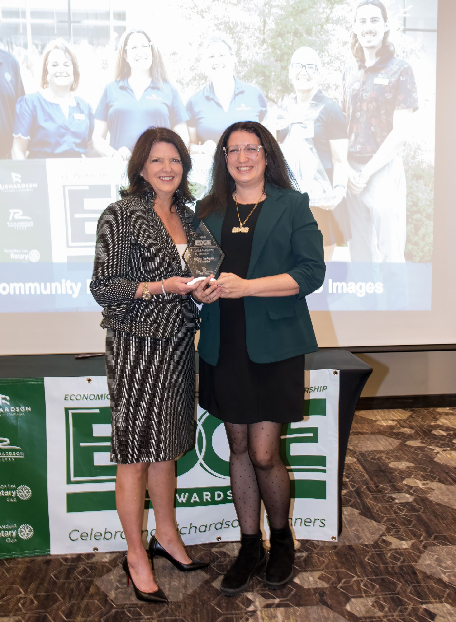 A group of people on a stage during an event, some waving and smiling, with a presentation screen in the background.