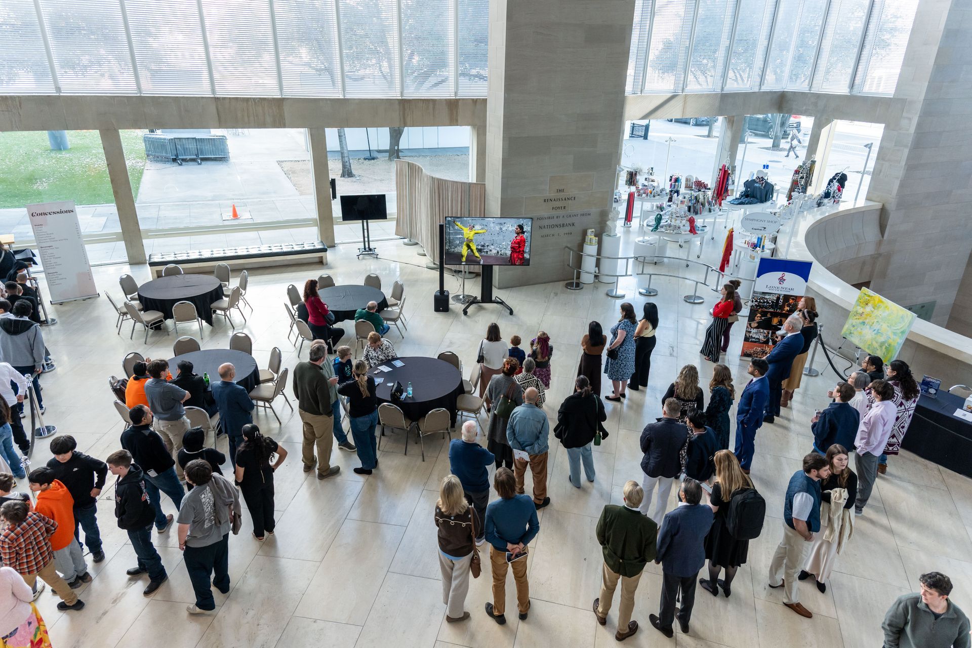 A high-angle view of an indoor event featuring guests standing in a large lobby and seated at round tables.
