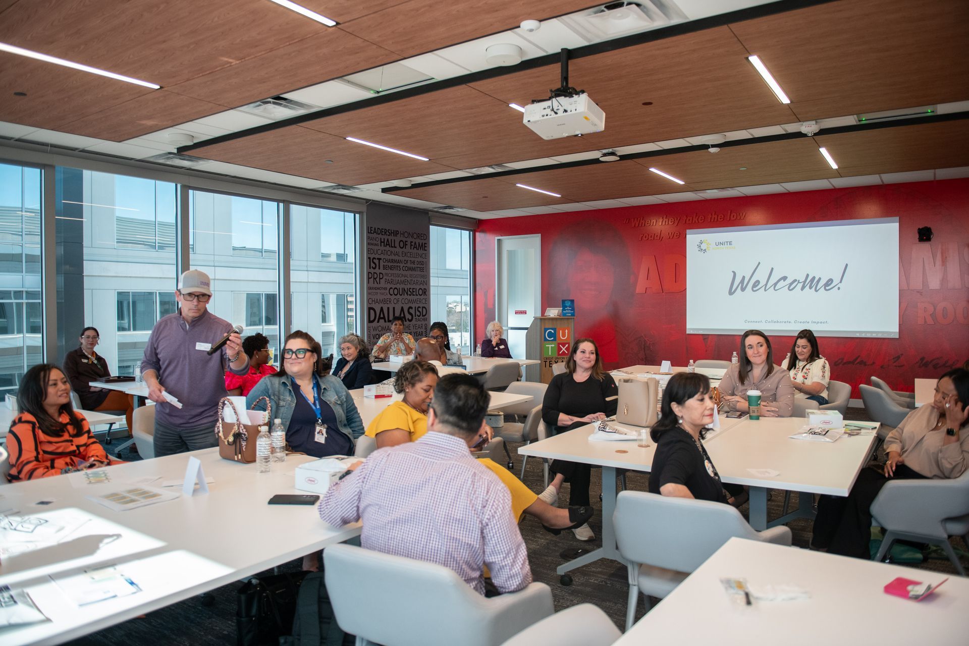 A group of people seated at tables in a modern, bright meeting room with a 
