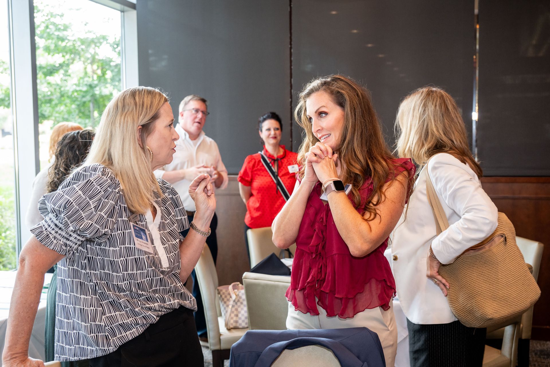 A group of people converse in an indoor setting, with three foreground individuals focused on each other.