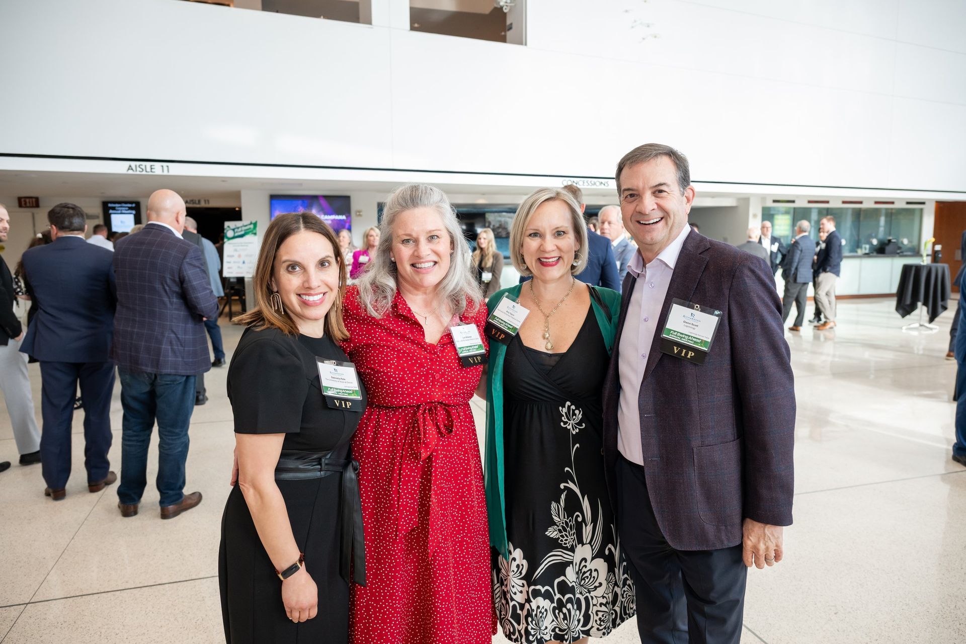 Four people smiling at a conference, posing in a bright, modern lobby with other attendees in the background.