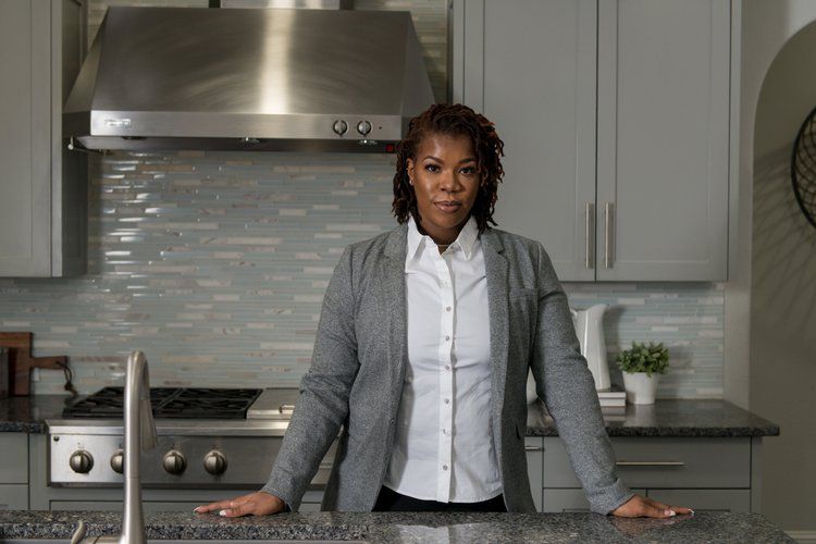A professional standing at a kitchen island, wearing a grey blazer and white shirt, with a modern kitchen in the background.