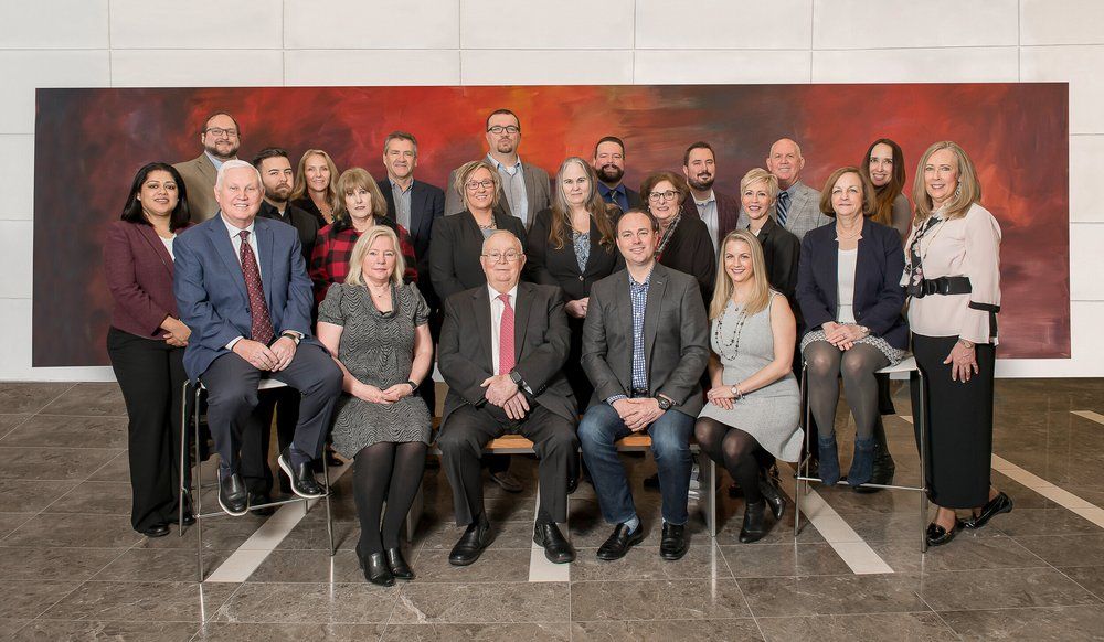 A group of professionals in business attire pose for a formal portrait in front of a large, abstract red wall painting.