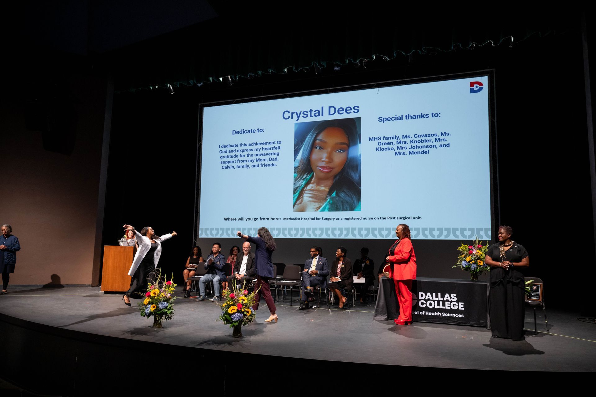 People on a stage at an event with a large screen displaying a biography of Crystalline Owen at Dallas College.