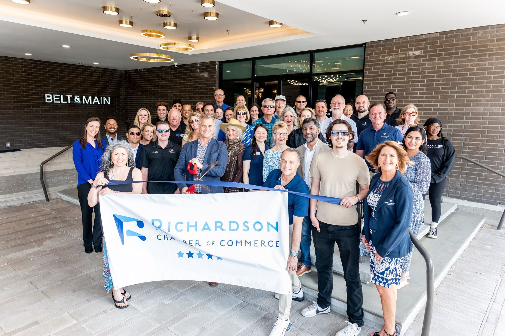 A group of people gathers in front of a building for a Richardson Chamber of Commerce ribbon-cutting ceremony.