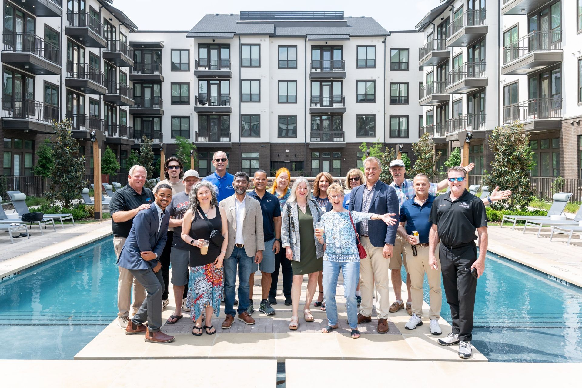 A group of people standing on a pool deck in front of a multi-story apartment building, posing for a photo.