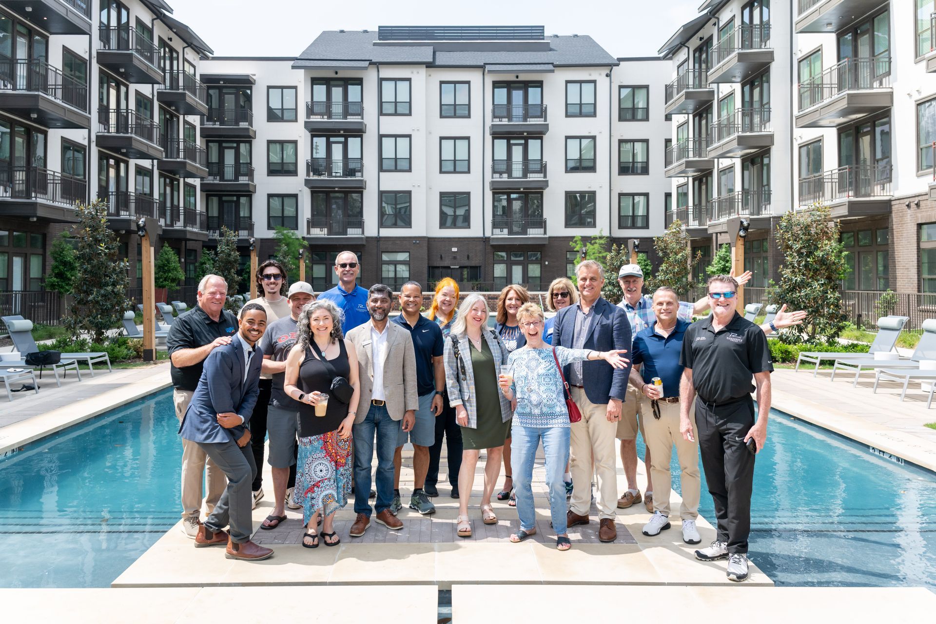 A group of people standing on a pool deck in front of a modern apartment complex.