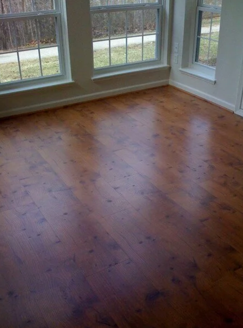 Hardwood floor in a room with large windows. The floor is reddish-brown and glossy.