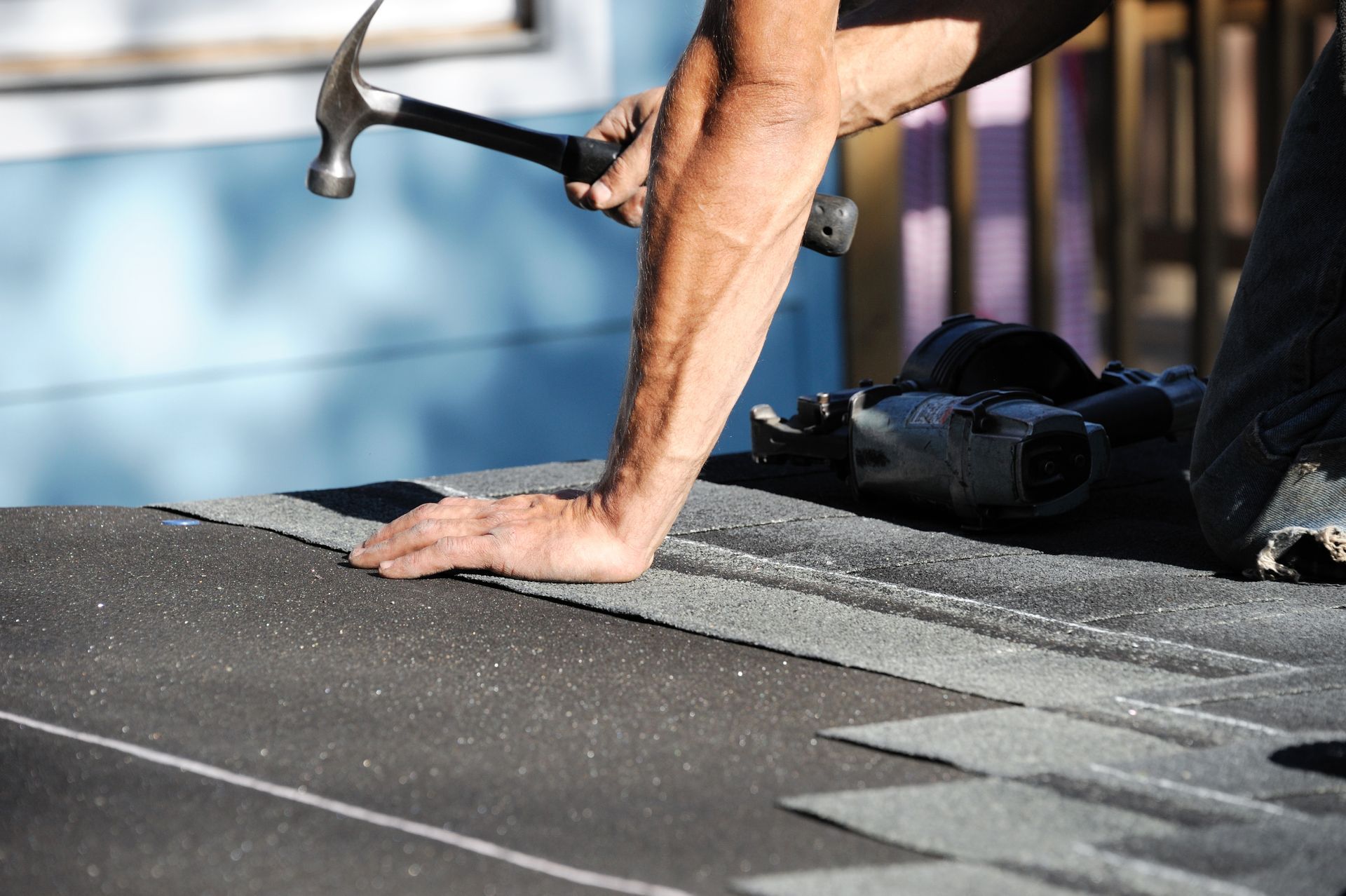 A man diligently repairs a roof, hammer in hand, surrounded by tools and roofing materials.