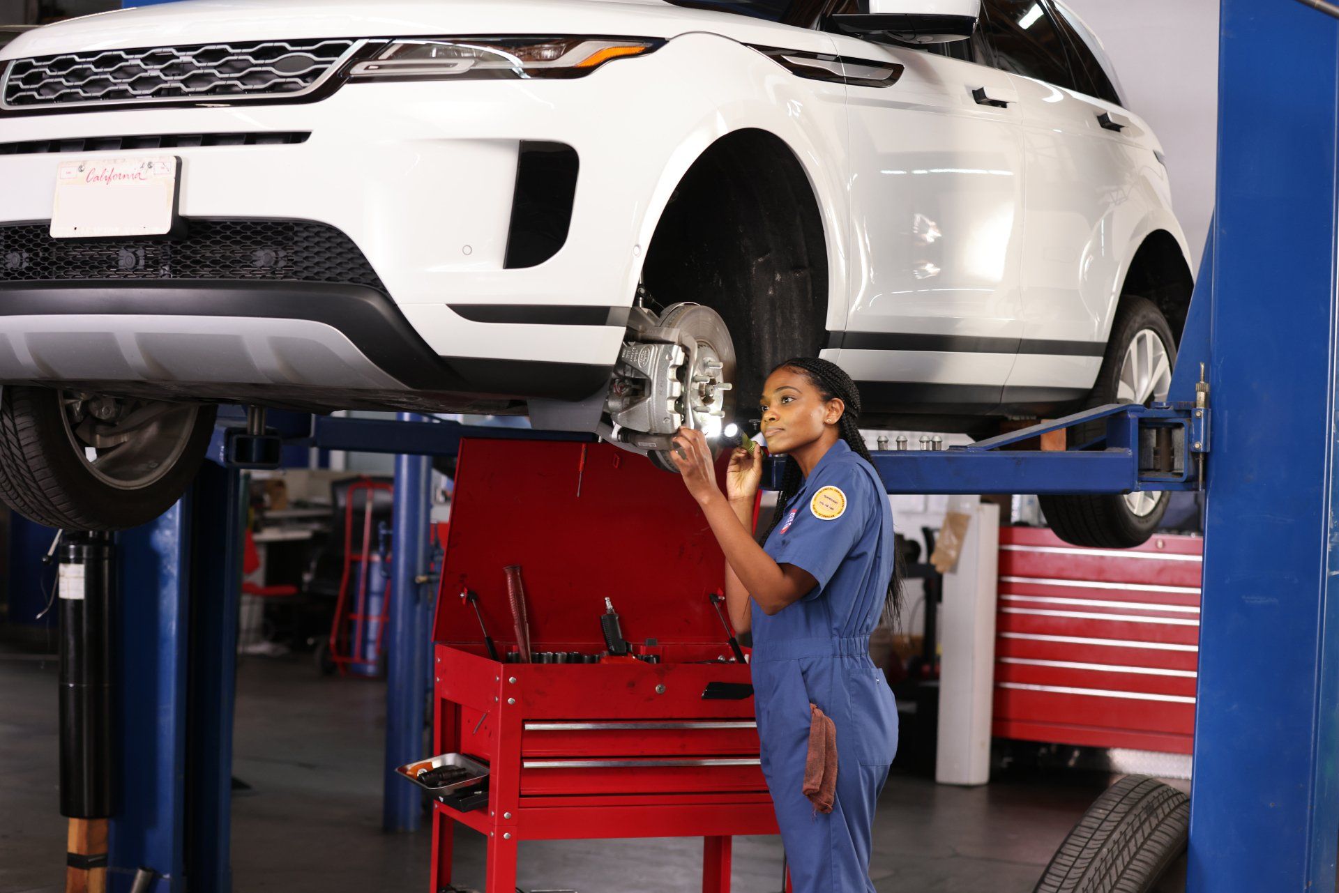 A woman is working on a car on a lift in a garage.