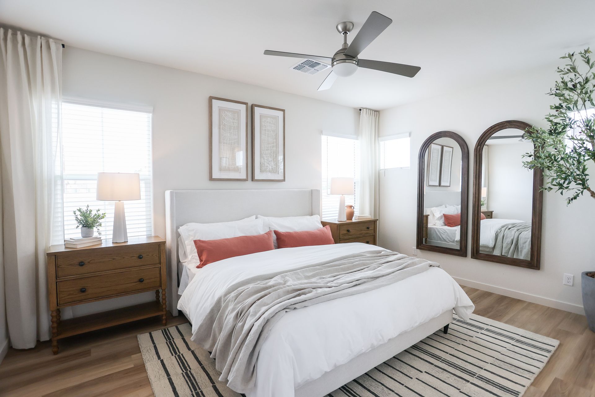 Bedroom with white bed, two arched mirrors, wood furniture, and neutral tones.