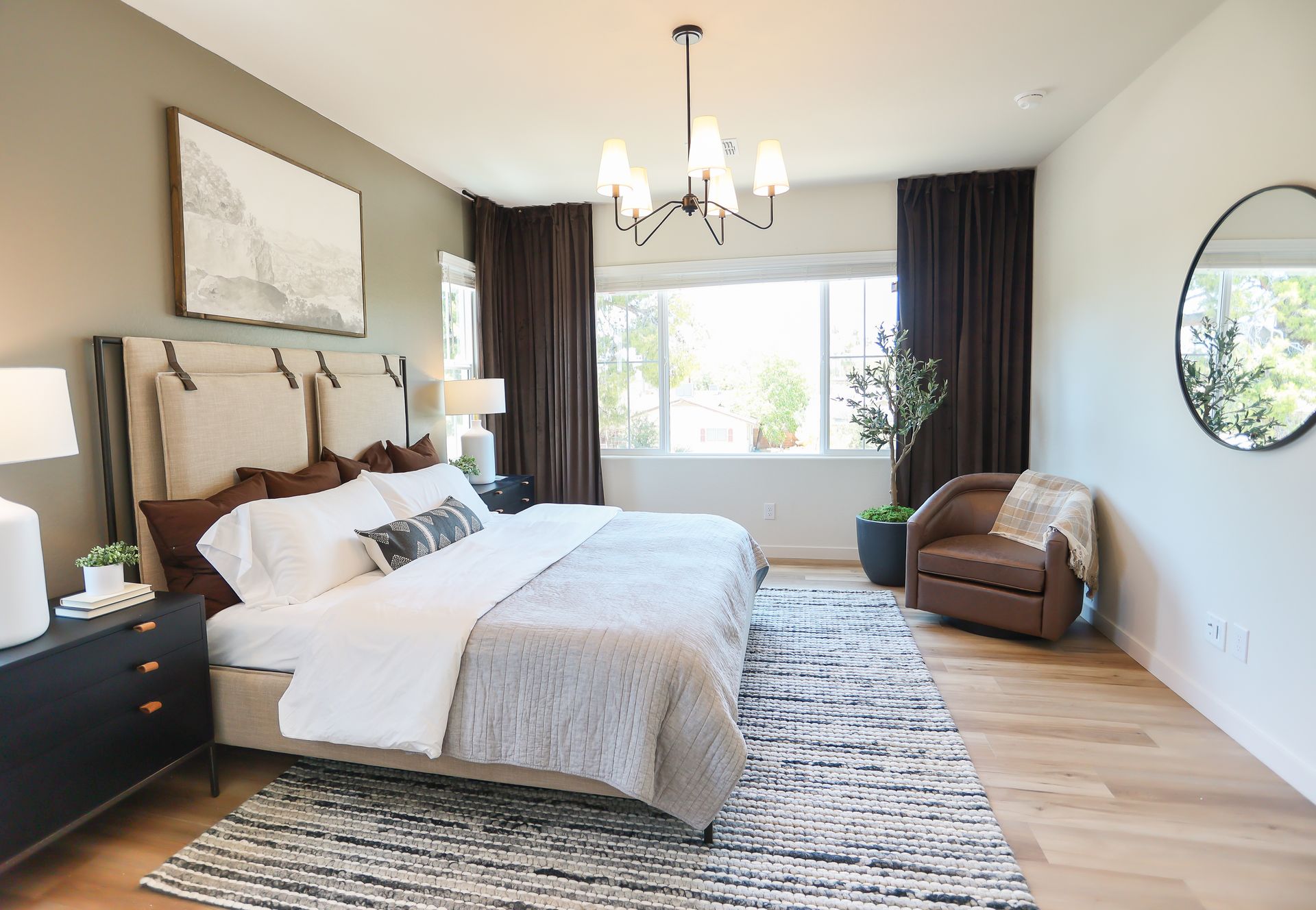 Bedroom with a large bed, brown curtains, and a chair. Neutral tones with a light-colored rug.