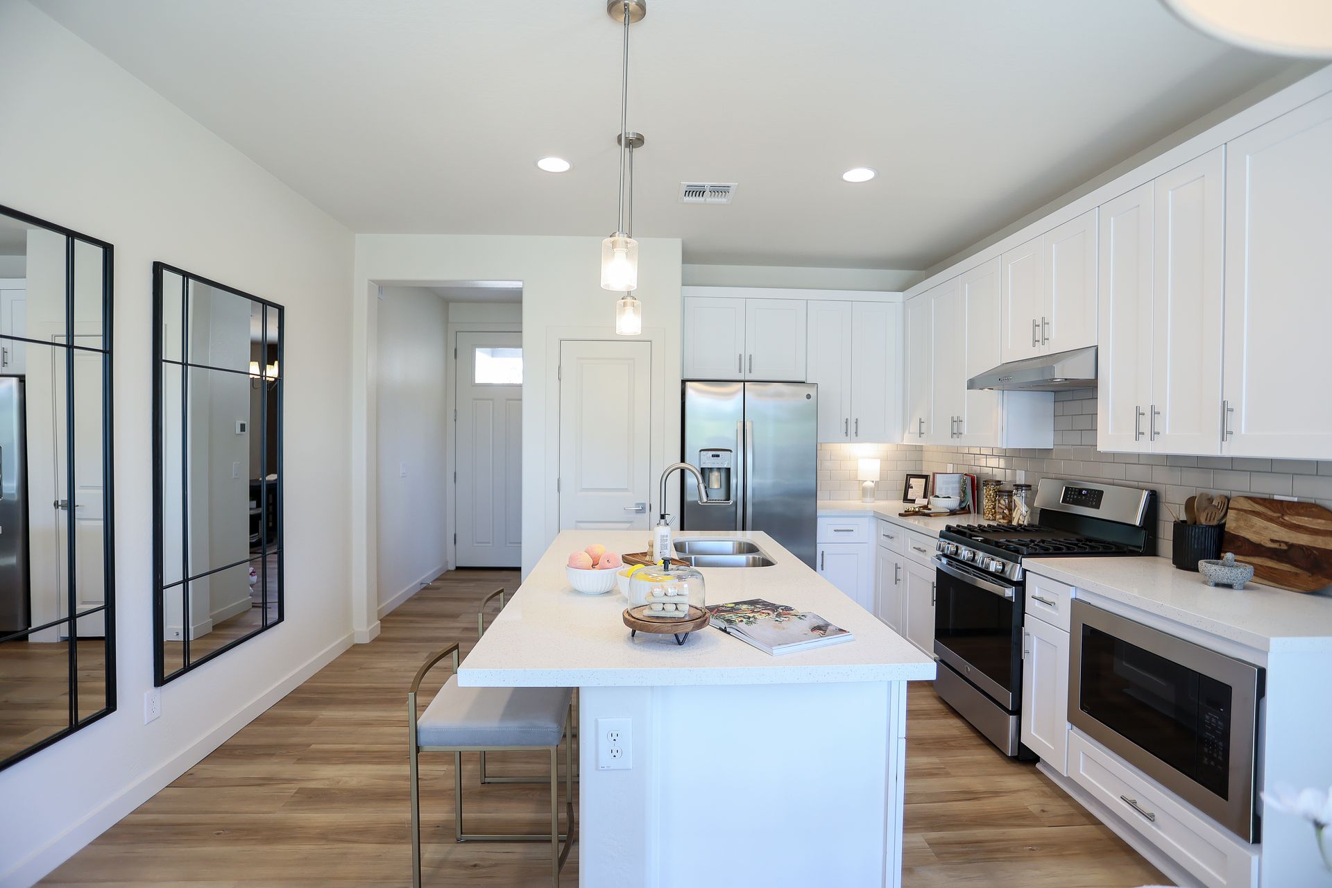 White kitchen with island, stainless steel appliances, and wood-look flooring. Two mirrors on wall.