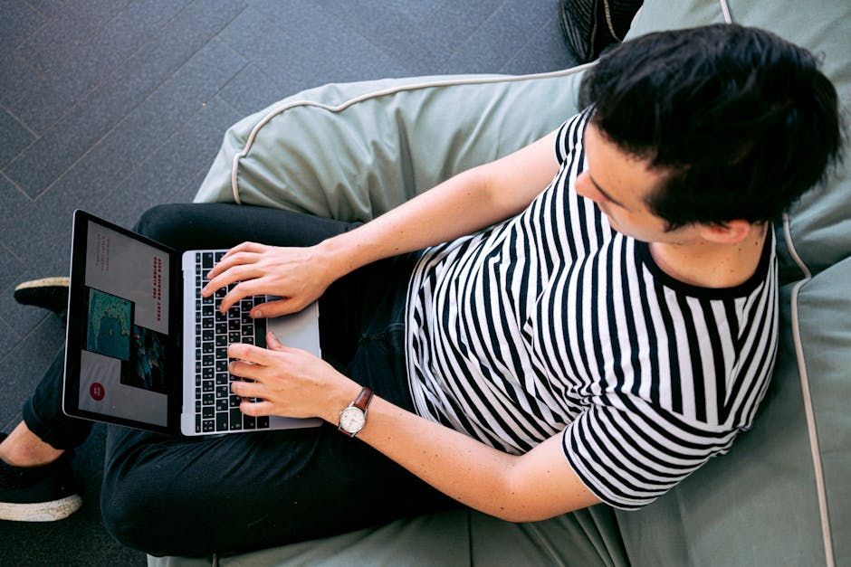 A man is sitting on a bean bag chair using a laptop computer.