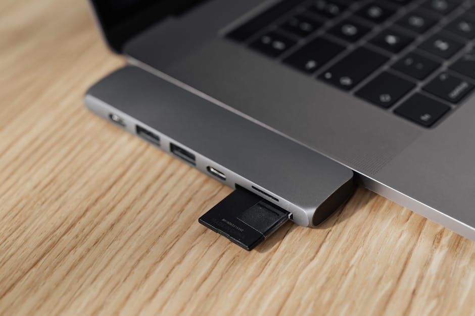 A laptop with a sd card plugged into it is sitting on a wooden table.